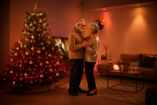 Prarodiče se objímají u vánočního stromku se smart světly Philips Hue Festavia, na stole jsou tradiční vánoční koláče v útulném obývacím pokoji. Prarodiče se objímají u vánočního stromku se smart světly Philips Hue Festavia, na stole jsou tradiční vánoční koláče v útulném obývacím pokoji.