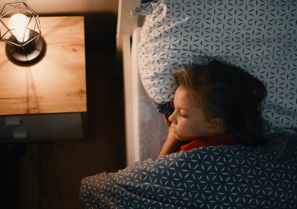 Chlapeček s hlavou na polštáři spící u světla lampy